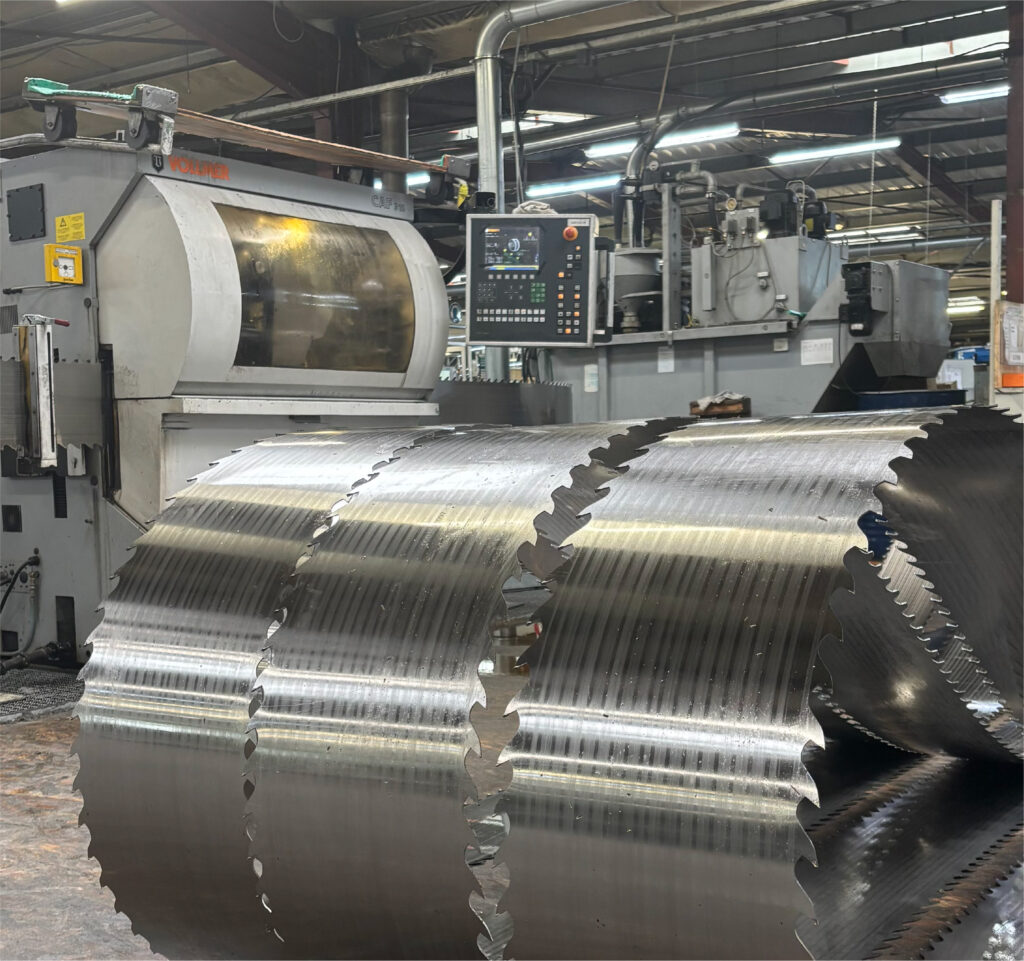 Coils of toothed steel band saw blades in front of an industrial production machine.