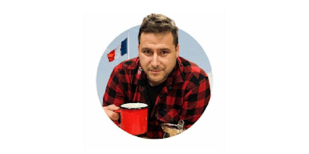 Laurent Jacquet, in a red-checked shirt, holding a red cup, in front of a wall decorated with flags