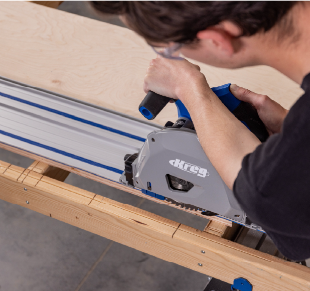 A man using a Kreg plunge saw on a guide rail for precise cutting of a wooden board.
