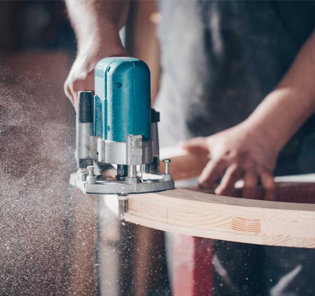Manual work with an electric router to shape a curved piece of wood.