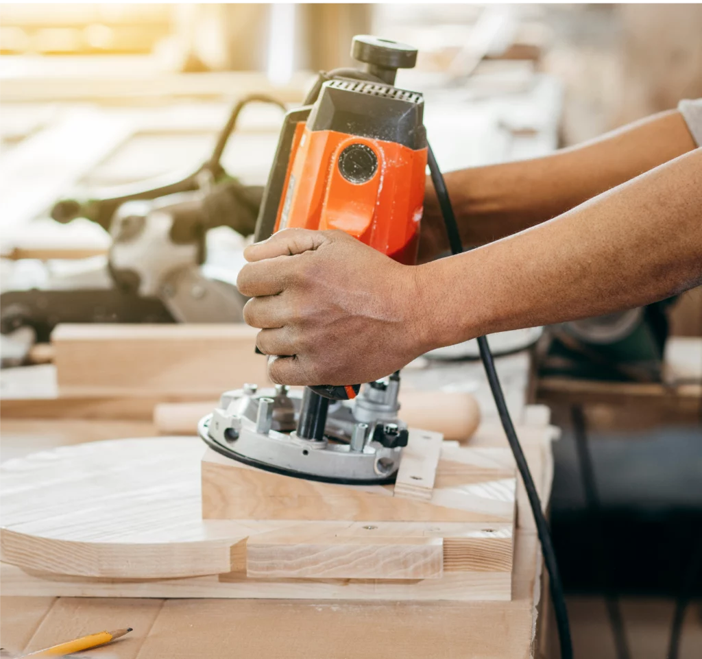 Joiner using an electric router to shape a piece of wood to measure.